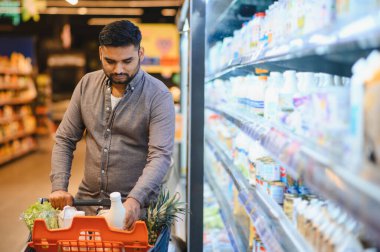 Marketten yiyecek alırken elinde süt şişesi tutan bir adam.