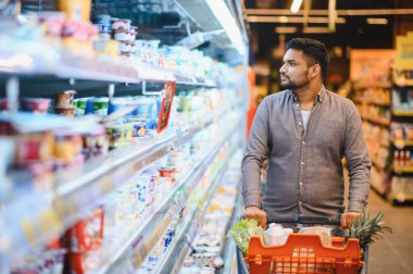 Süpermarketteki soğutulmuş raflardan ürün seçerken market arabasını iten bir adam. Günlük rutin, yiyecek alışverişi konsepti.