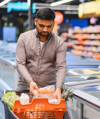 Sağlıklı yiyecek almak için alışveriş yapan, bulanık süpermarket koridorunda turuncu alışveriş arabasına taze somon koyan bir adam.