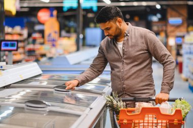 Marketteki dondurucudan dondurulmuş ürünlere uzanan adam. Çeşitli seçeneklerden ögeler seçmekle meşgul tüketici