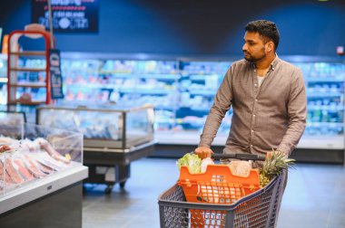 Modern bir markette ürünleri seçerken içi taze ürünlerle dolu bir alışveriş arabasını iten adam.