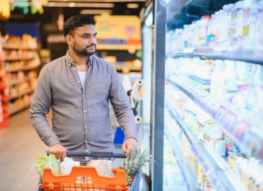 Süpermarkette alışveriş arabasını iten, soğutulmuş raflardan ürün seçen bir adam. Günlük rutin ve perakende deneyimi
