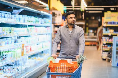 Adam market alışverişi yapıyor, market koridorlarında alışveriş yapıyor, ev için gıda ürünleri seçiyor.