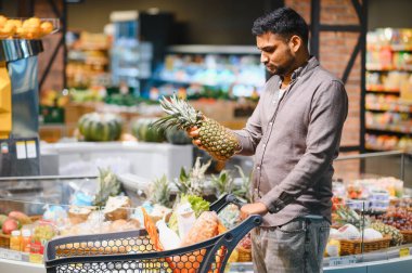 Elinde taze ananas tutan bir adam, markette sebze reyonunu seçen, modern, iyi stoklanmış bir süpermarkette