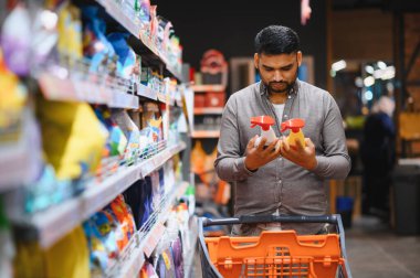 Elinde iki farklı deterjan şişesi tutan bir adam markette satın alma kararı veriyor.
