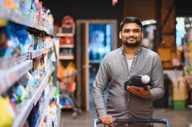 Gülümseyen, temizlik malzemesi tutan, markette alışveriş arabası süren, ev eşyaları için alışveriş yapan bir adam.