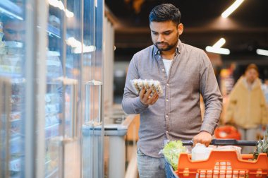 Market alışverişi yapan, süpermarket koridorunda taze gıda paketlerini inceleyen, sağlıklı ürünleri seçen bir adam.