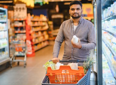 Süpermarkette taze ürün bulan bir adam, ürünlerle dolu bir alışveriş arabasını iten, süt ürünlerini seçen bir adam.