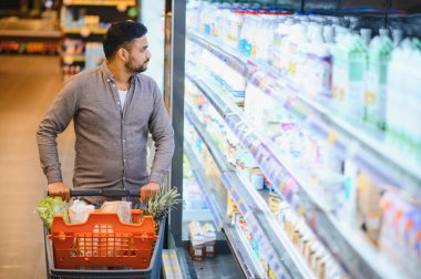 Marketteki marketin buzdolabındaki mandıra ürünlerine bakan bir adam alışveriş arabasını itiyor.