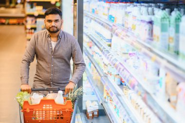 Market alışverişi, mandıra koridorunda dolu bir sepeti itmek. Ürün seçen günlük tüketici