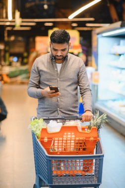 Alışveriş arabası satan adam akıllı telefonundaki fiyatları ve ürünleri modern bir alışveriş deneyimi için karşılaştırıyor.