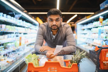 Markette kağıt alışveriş makbuzuna bakan bir adam, artan gıda maliyetleri ve tüketici harcamaları hakkında endişeli hissediyor