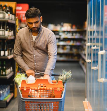 Taze ürünler ve paketlerle dolu alışveriş arabalarını iten adam süpermarket koridorlarında yürüyor.