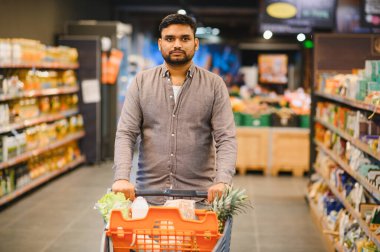 Süpermarket koridorlarında alışveriş arabalarını iten adam, günlük tüketim ve perakendeciliğe odaklanıyor.