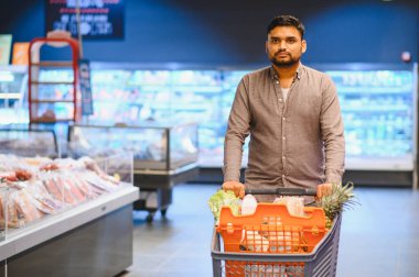 Müşteri ürünleri seçiyor ve alışveriş arabasıyla dolu bir süpermarket koridorundan geçiyor.