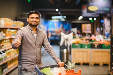 Kendine güveni tam bir adam, alışveriş arabasıyla alışveriş yapıyor ve modern bir perakende ortamından tatmin oluyor.