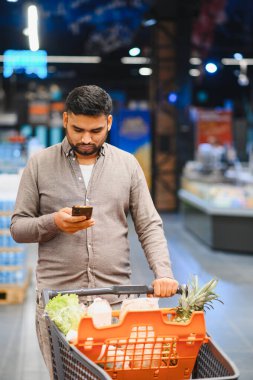Marketteki akıllı telefonların ürünlerini ve fiyatlarını karşılaştıran alışveriş arabalarını iten genç bir adam.