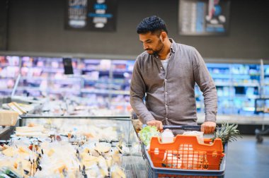Taze ürünlerle dolu alışveriş arabasını iten adam soğutulmuş vitrinden ürünler seçiyor.