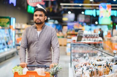 Alışveriş arabasını iten bir adam markette alışveriş arabasıyla doğrudan kameraya bakıyor.