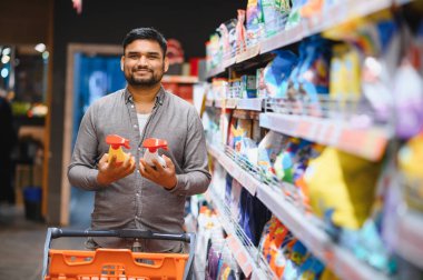 Markette elinde iki şişe sprey tutan adam, alışveriş yaparken temizlik ürünleri arasında seçim yapıyor.