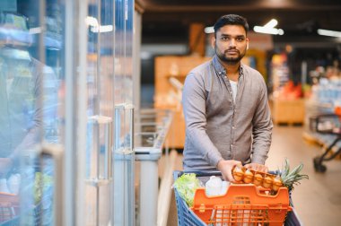 Market koridorunda alışveriş yapan, yumurta alan ve taze üretim yapan genç bir adam, tüketim kavramı
