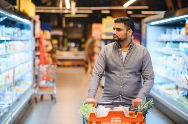 Market alışverişini seçen, dondurulmuş koridorda turuncu bir alışveriş arabasını iten, perakende ve tüketici seçimlerine odaklanan bir adam.