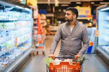 Süpermarket koridorlarında alışveriş arabası süren bir adam sağlıklı günlük yaşam tarzı ve market rutini için taze ürünler seçiyor.