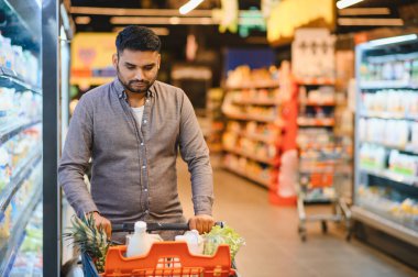 Markette yiyecek alışverişi yapan bir adam, ananas, süt ve marul gibi ürünlerle dolu bir arabayı iten bir adam.
