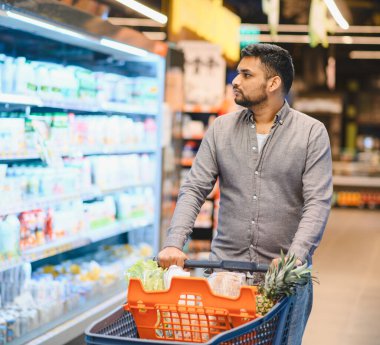 Müşteri taze yiyecek ve ürünleri raflardan seçiyor, modern bir market koridorunda satın alma kararları alıyor.