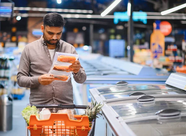 Elinde bir paket somon fileto tutan bir adam markette alışveriş için karar veriyor.