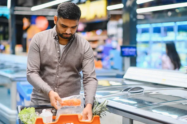 Modern bir süpermarkette alışveriş yaparken paketlenmiş somon tutan adam. Sağlıklı beslenmeye ve tüketici seçimlerine odaklan
