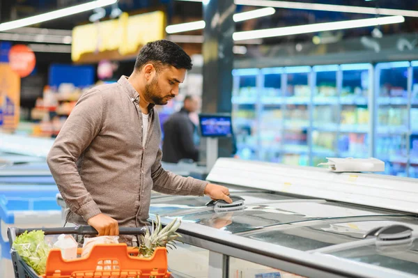 Müşteri dondurucudan ürünleri seçerken market arabasını taze ürünlerle dolduruyor ve günlük ihtiyaçlara odaklanıyor.