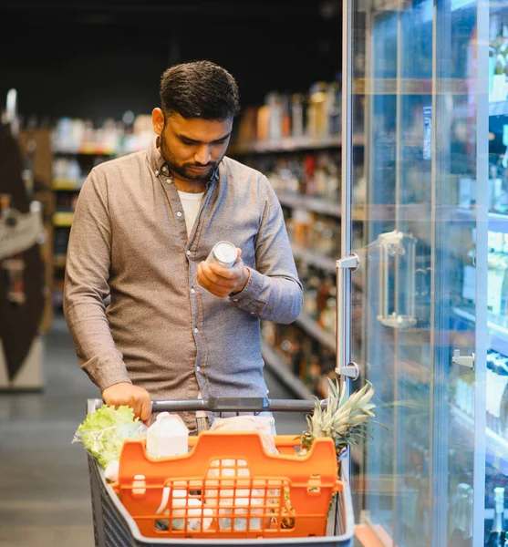 Genç adam, modern bir markette yiyecek ve içecek alırken ürün etiketi detaylarını okuyor.