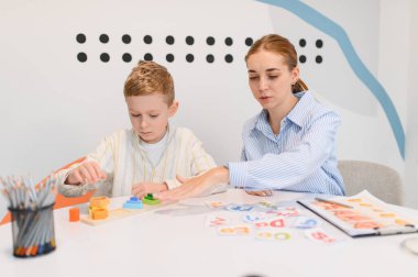 Eğitim oyuncakları ve alfabe kartlarıyla oynayan genç bir çocuk, bir bayan öğretmenden yardım alıyor. Çocuk gelişimi ve okur yazarlığa odaklanma