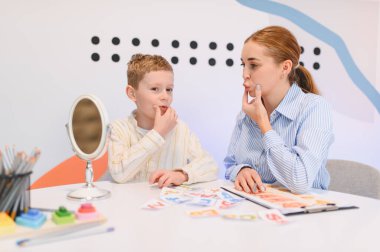 Konuşma terapisti ve çocuk bir klinikte ayna ve eğitim materyalleri kullanarak konuşma egzersizleri yapıyor.