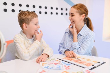 Konuşma terapisti ve çocuk yüz yüze konuşma egzersizleri yapıyor, görsel araçlarla düzgün ağız hareketleri öğreniyorlar.