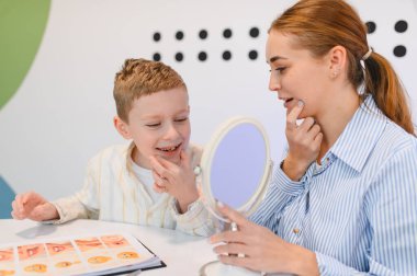 Konuşma terapisti genç bir çocukla konuşma düzeltme ve dil geliştirme için ayna kullanarak konuşma egzersizleri yapıyor.