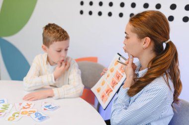 Bir klinikte dil geliştirme oturumu sırasında genç bir çocuğa konuşma egzersizleri konusunda rehberlik eden bir kadın konuşma terapisti.