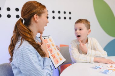 Konuşma terapisti kadın ve genç çocuk ıslah eğitimi sırasında konuşma dili öğreniyorlar. Çocuk görsel yardımdan ağız pozisyonlarını tekrarlıyor
