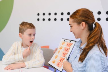 Konuşma terapisti, öğrenme terapisi sırasında yüz ifadesi grafiği kullanarak eklem egzersizleri yapan bir çocuğa yardım ediyor.