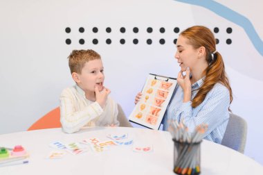 Konuşma terapisti genç bir çocukla çalışıyor, görsel araçlar kullanarak konuşma eklemlerini geliştirmesine yardım ediyor ve etkinlikleri etkiliyor.