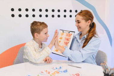 Genç bir çocuk konuşma terapisi seansına katılıyor. Terapistten öğreniyor. Cesaret ve pozitif destek için beşlik çakıyor.