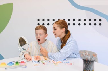 Genç bir çocuk, kadın uzmanla konuşma terapisi sırasında seslendirme ve telaffuz pratiği yapıyor.