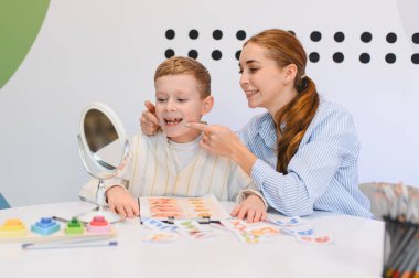 Çocuk, aynanın önünde bir logopediciyle ağız ve dil egzersizlerini tekrarlayarak konuşma ve iletişim becerilerini geliştiriyor.