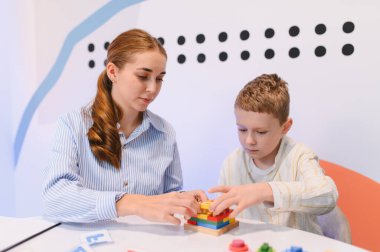 Eğitimci, rehabilitasyon ortamında iyi motor beceriler ve bilişsel beceriler geliştiren terapi blokları olan genç bir çocuğa yardım ediyor.