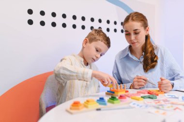 Eğitimsel oyuncaklarla uğraşan, iyi motor beceriler geliştiren ve bir öğretmenle problem çözen bir çocuk.