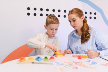 Genç bir çocuk renkli tahta bloklarla gelişim oyunu oynuyor. Kadın bir öğretmenle mantık ve koordinasyonu geliştiriyor.