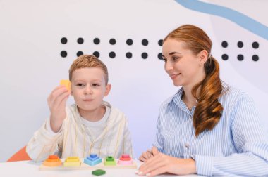 Renkli tahta istif taşlarıyla oynayan, iyi motor beceriler geliştiren ve bir öğretmenin rehberliğinde problem çözen bir çocuk.