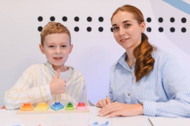 Terapistle oynanan eğitim oyununda başarı ve onay gösteren çocuk, sınıf ortamında beceri geliştirme