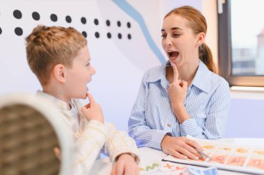 Konuşma terapisti bir çocuğa seans sırasında yardım ediyor, konuşma becerilerini geliştirmek ve dil gelişimi için iletişim becerilerini geliştiriyor.